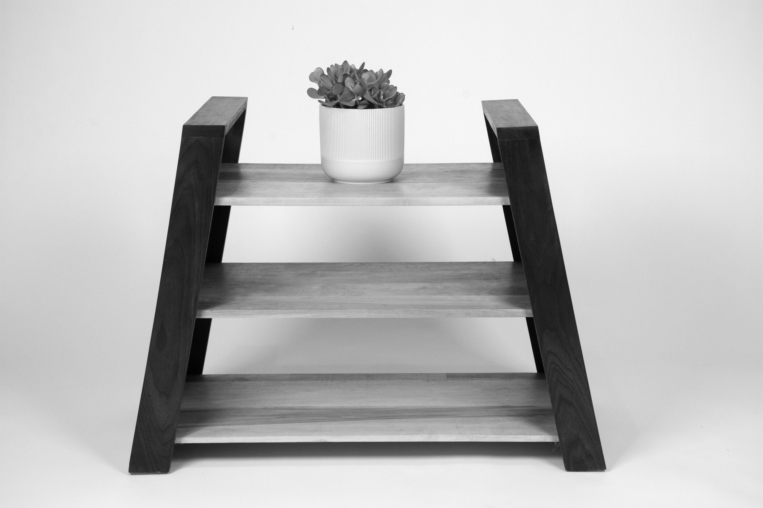 black and white image of a 3 shelved table with a pot on top